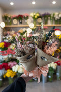 Bouquet of dried flowers in a textured paper wrap held by a person against a white background
