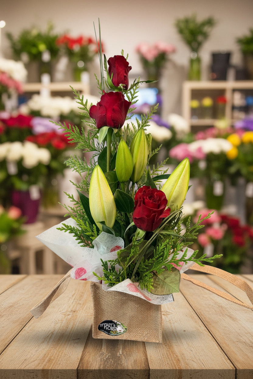 Bouquet of red roses and yellow lilies in a decorative paper and burlap bag on a white background