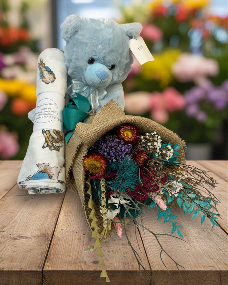 Blue teddy bear with a bouquet of flowers and a baby blanket on a white background