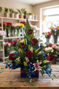 Floral arrangement with red roses, green leaves, and pink lilies in a blue box on a white background
