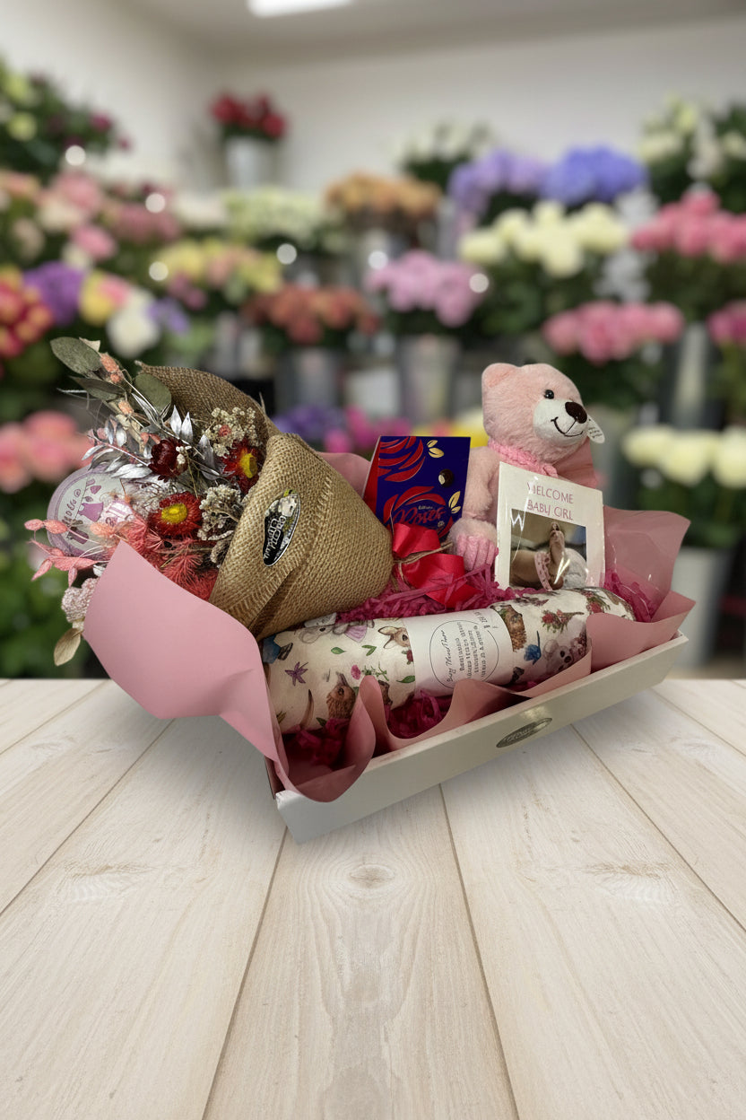 Gift box with flowers, teddy bear, and wrapped items on a white background