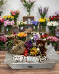 Gift basket with a teddy bear, flowers, and wrapped items on a white background