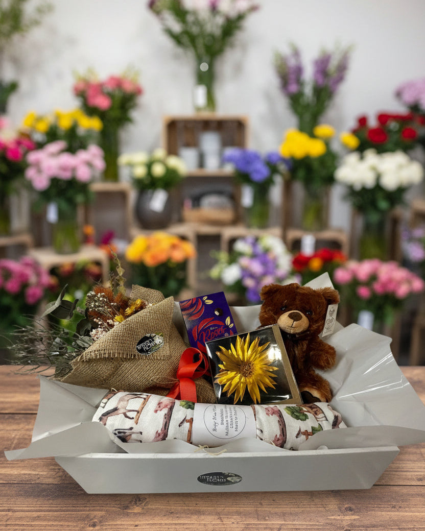 Gift basket with a teddy bear, flowers, and wrapped items on a white background