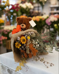 Teddy bear with a bouquet of flowers and a tag on a white background