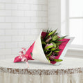 Bouquet of flowers wrapped in pink paper with a white ribbon on a white background
