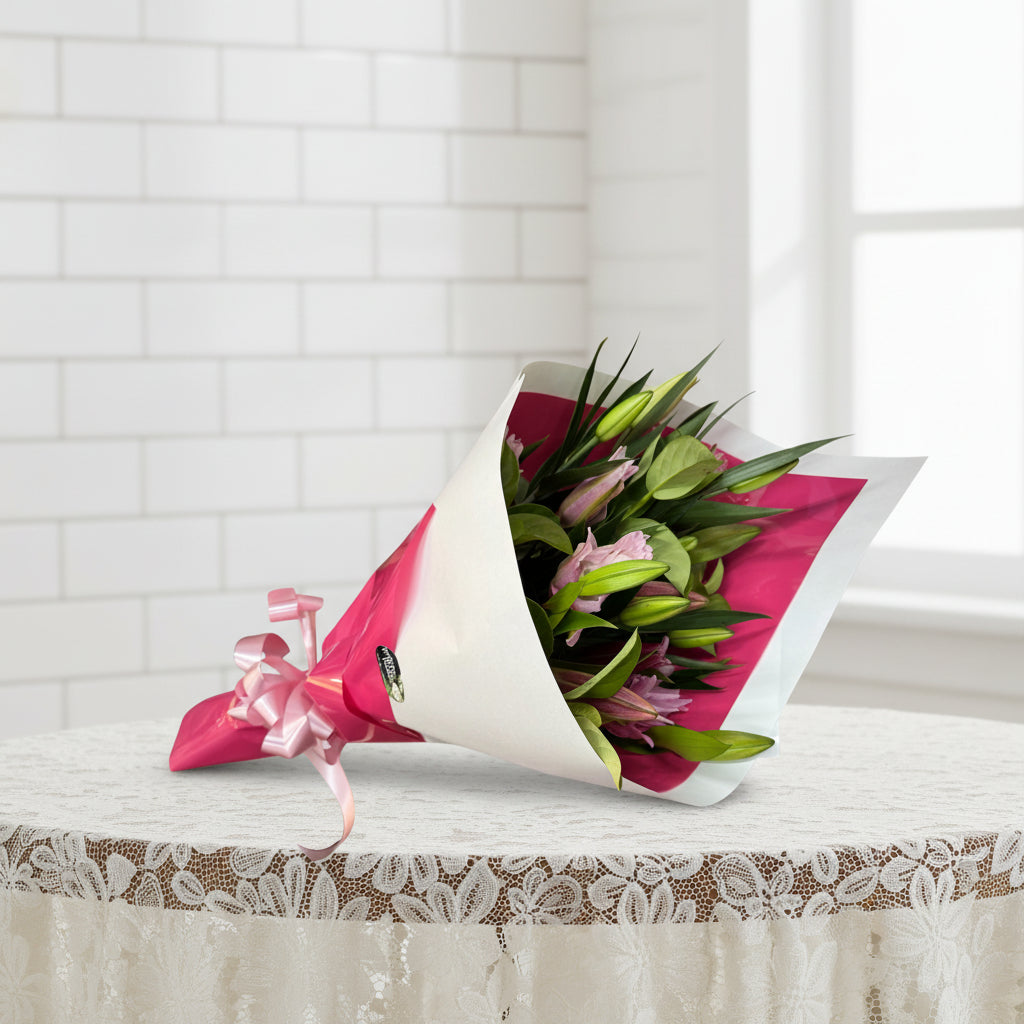 Bouquet of flowers wrapped in pink paper with a white ribbon on a white background