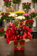 A festive Grinch-themed candy bouquet gift set in a red box with a large red bow, filled with assorted chocolate bars and wrapped in red and green tissue paper.