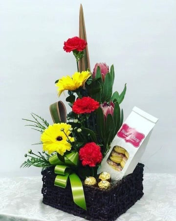 Floral arrangement with a gift box and a packet of cookies on a white background
