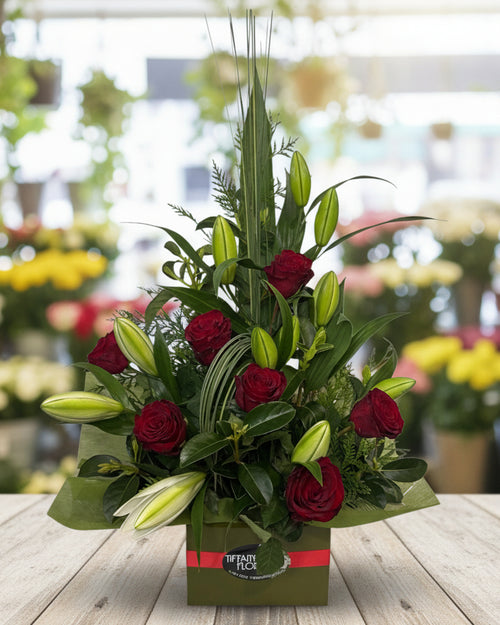 Floral arrangement with red roses and greenery in a box on a white background