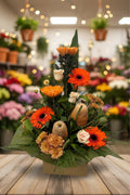 Floral arrangement with orange and red flowers, green leaves, and decorative elements in a box on a white background.