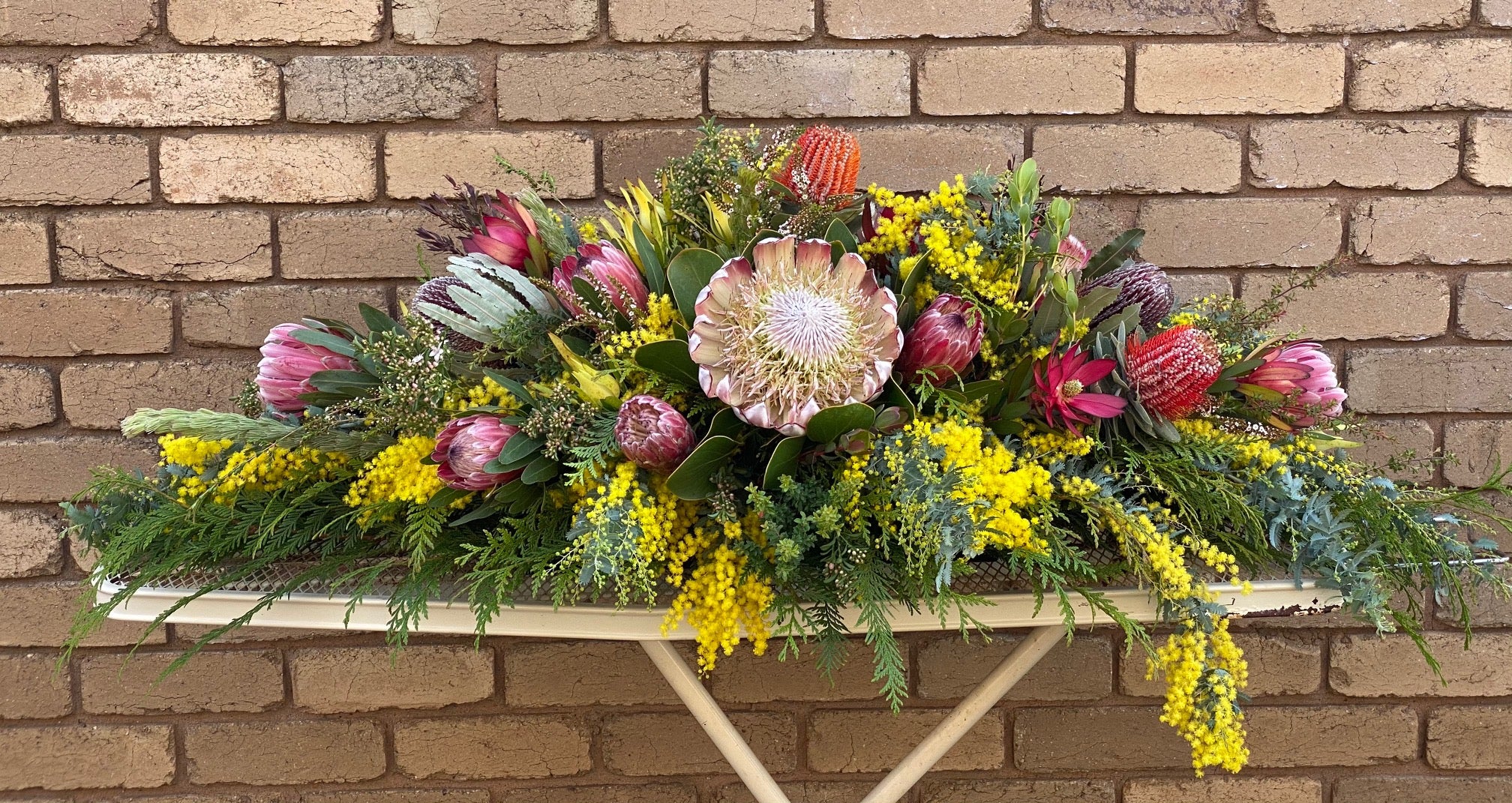 Floral arrangement on a wooden shelf against a brick wall